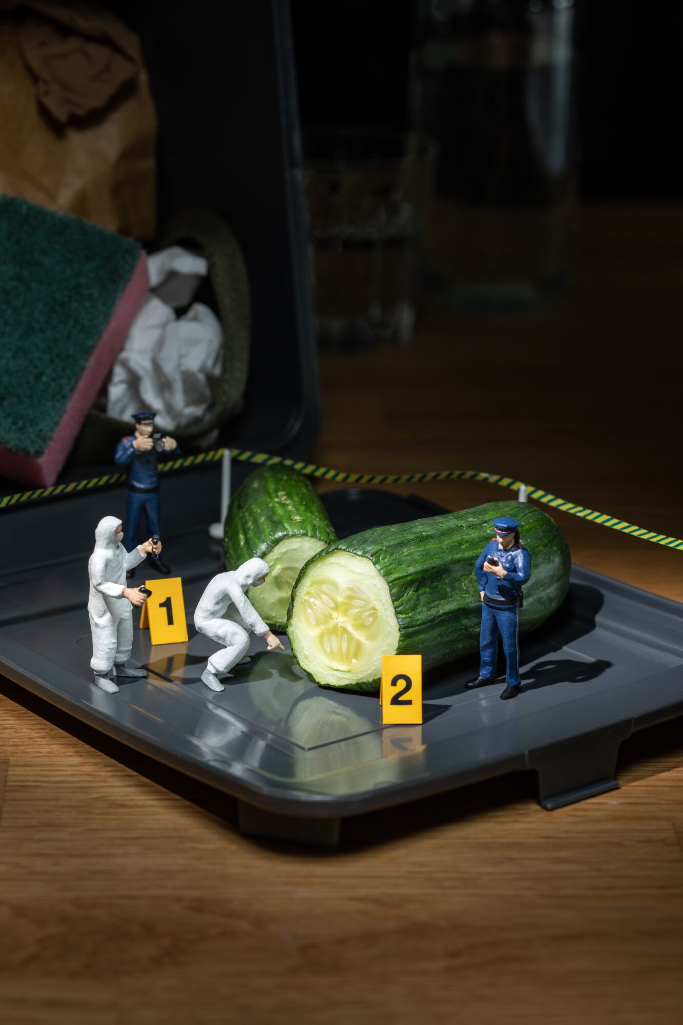 Miniaturpolizisten inspizieren den Tatort Tonne mit Gurken.