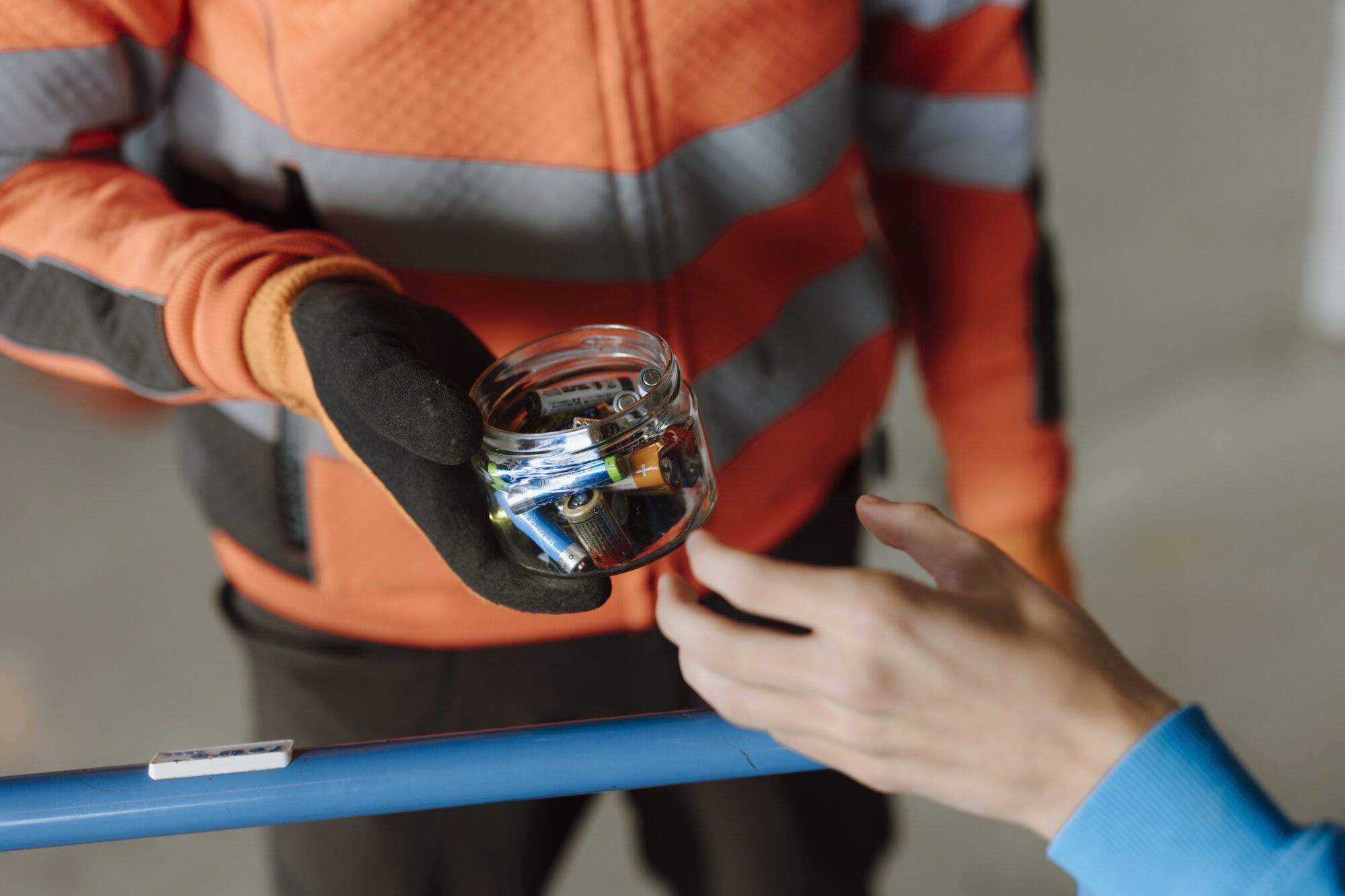 Man sieht die &Uuml;bergabe eines Vorratsglases, das Batterien beinhaltet.