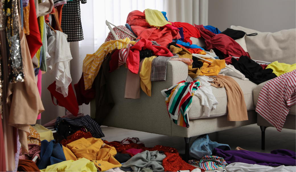 Auf dem Foto sieht man Berge von Damenkleidung, die auf einem Sofa las auch am Boden herumliegen.