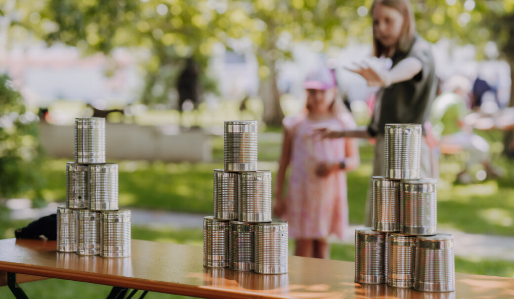 Eine Praktikantin erkl&auml;rt einem Kind ein Dosenwerfspiel.