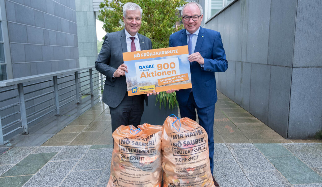 Das Bild zeigt zwei ältere Männer im Anzug mit einer Tafel in der Hand auf der steht: NÖ Frühjahrsputz. Danke für knapp 900 Aktionen. Vor den Männer sieht man noch zwei gefüllte orange Müllsäcke.