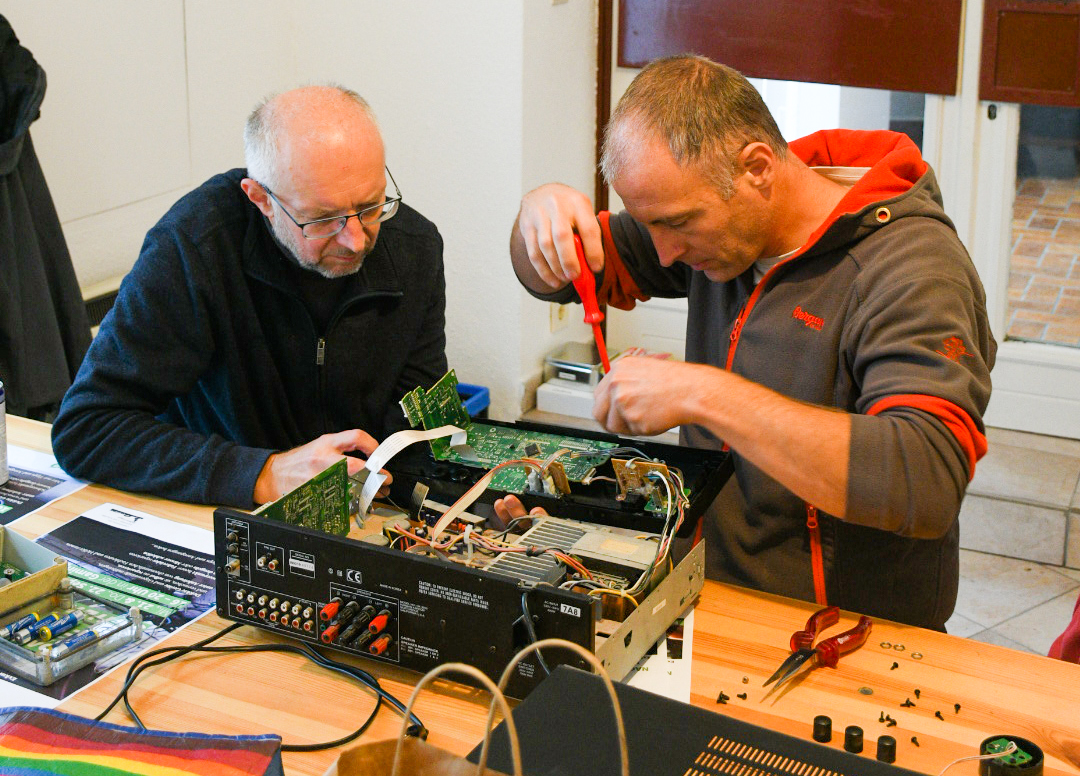 Auf dem Foto sieht man zwei Männer, die gerade ein elektronisches Gerät reparieren.