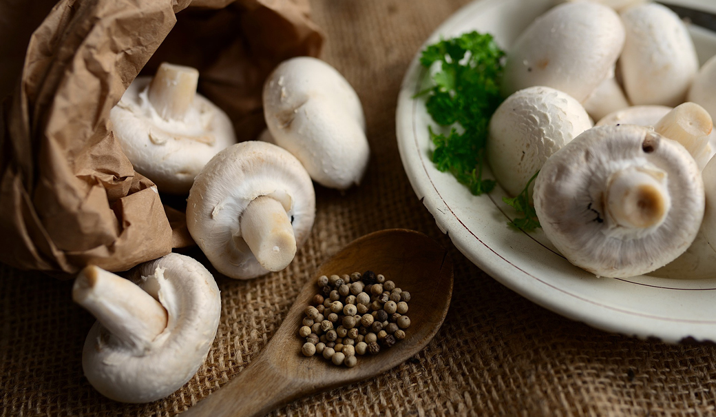 Weiße Champignons auf einem rustikalen Teller, daneben ein Holzlöffel mit Gewürzen